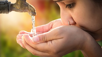 Moça tomando água direto da torneira com as mãos 